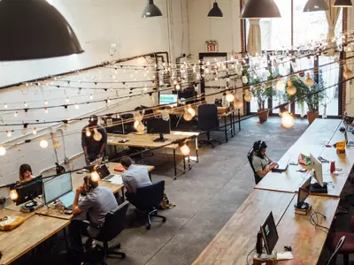 A big office space with wooden desks and a lot of lightbulbs. I'm glad I don't have to pay their energy bill.